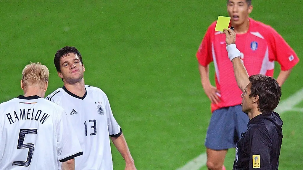 Der-Schweizer-Schiedsrichter-Urs-Meier-r-vorn-zeigt-dem-deutschen-Mittelfeldspieler-Michael-Ballack-2-v-l-die-Gelbe-Karte-An-Ballacks-Seite-Carsten-Ramelow-l-Die-deutsche-Fussballnationalmannschaft-gewinnt-am-25-06-2002-in-Seoul-das-Halbfinalspiel-des-17-WM-Turniers-gegen-die-Elf-des-Gastgebers-Suedkorea-durch-Ballacks-Tor-mit-1-0-und-qualifiziert-sich-damit-zum-siebentenmal-fuer-das-Endspiel-in-dem-Ballack-nach-seiner-zweiten-Gelben-Karte-fehlt