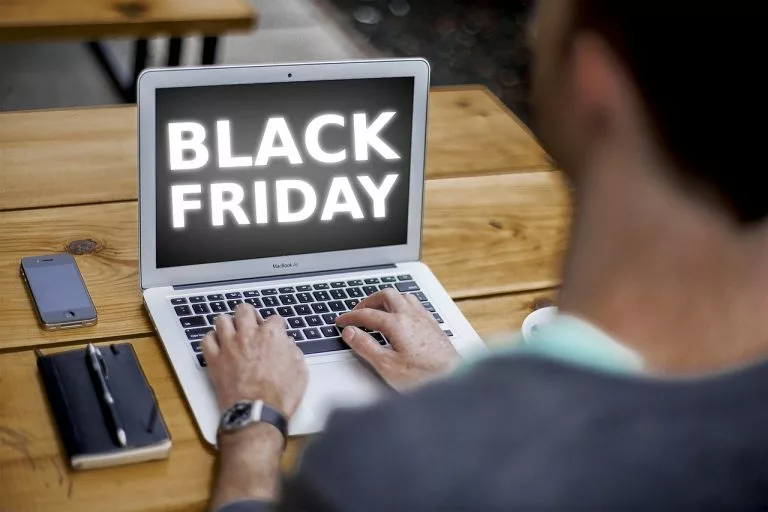 Auf einem Schreibtisch steht ein Laptop, auf dem ein Mann tippt. Auf dem Bildschirm stehen die Worte âÂÂBlack FridayâÂÂ.
